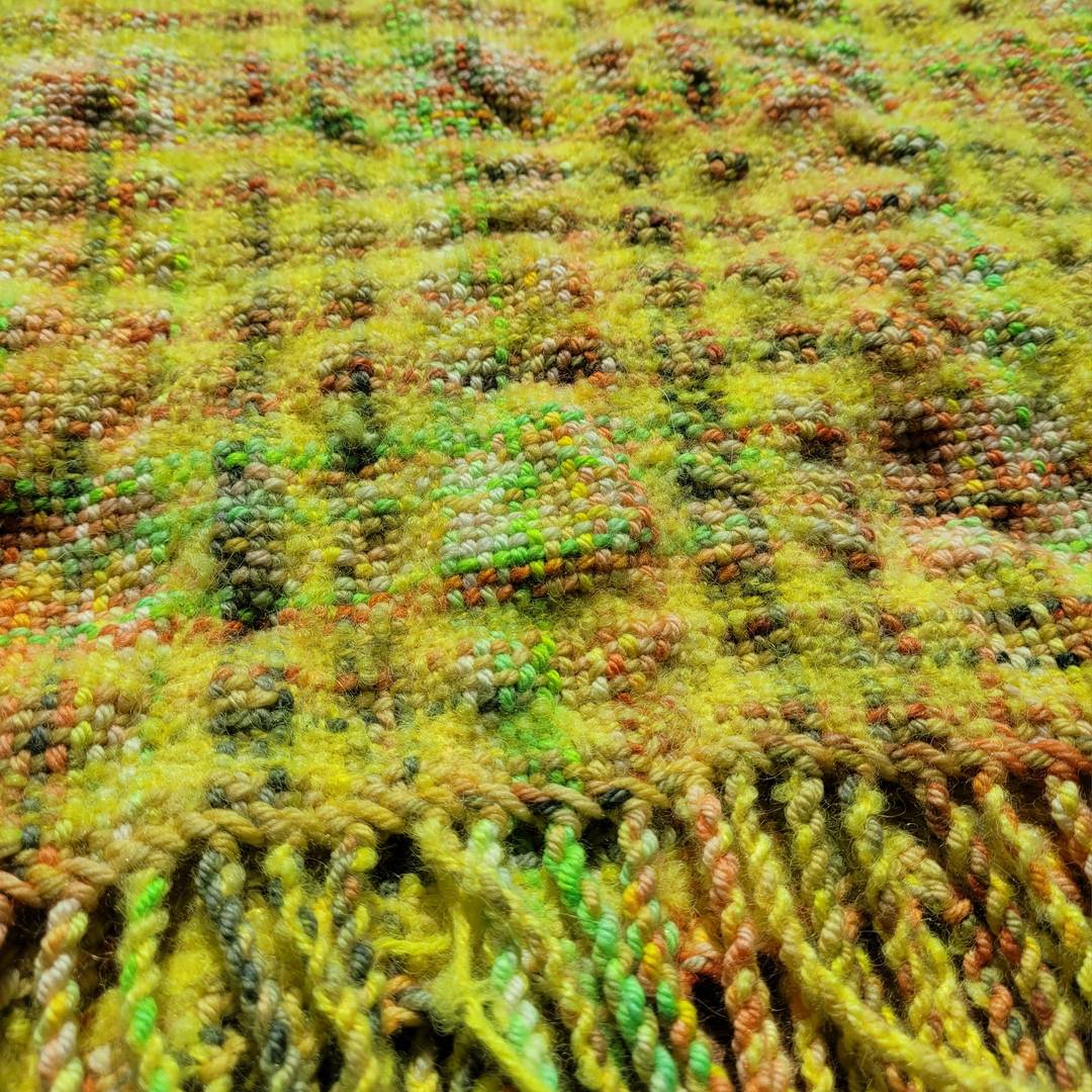 Mostly-yellow plaid scarf with variegated yellow/green/orange blips throughout. Scarf has experienced differential shrinkage, so parts of it are felted and puckered compared to others.