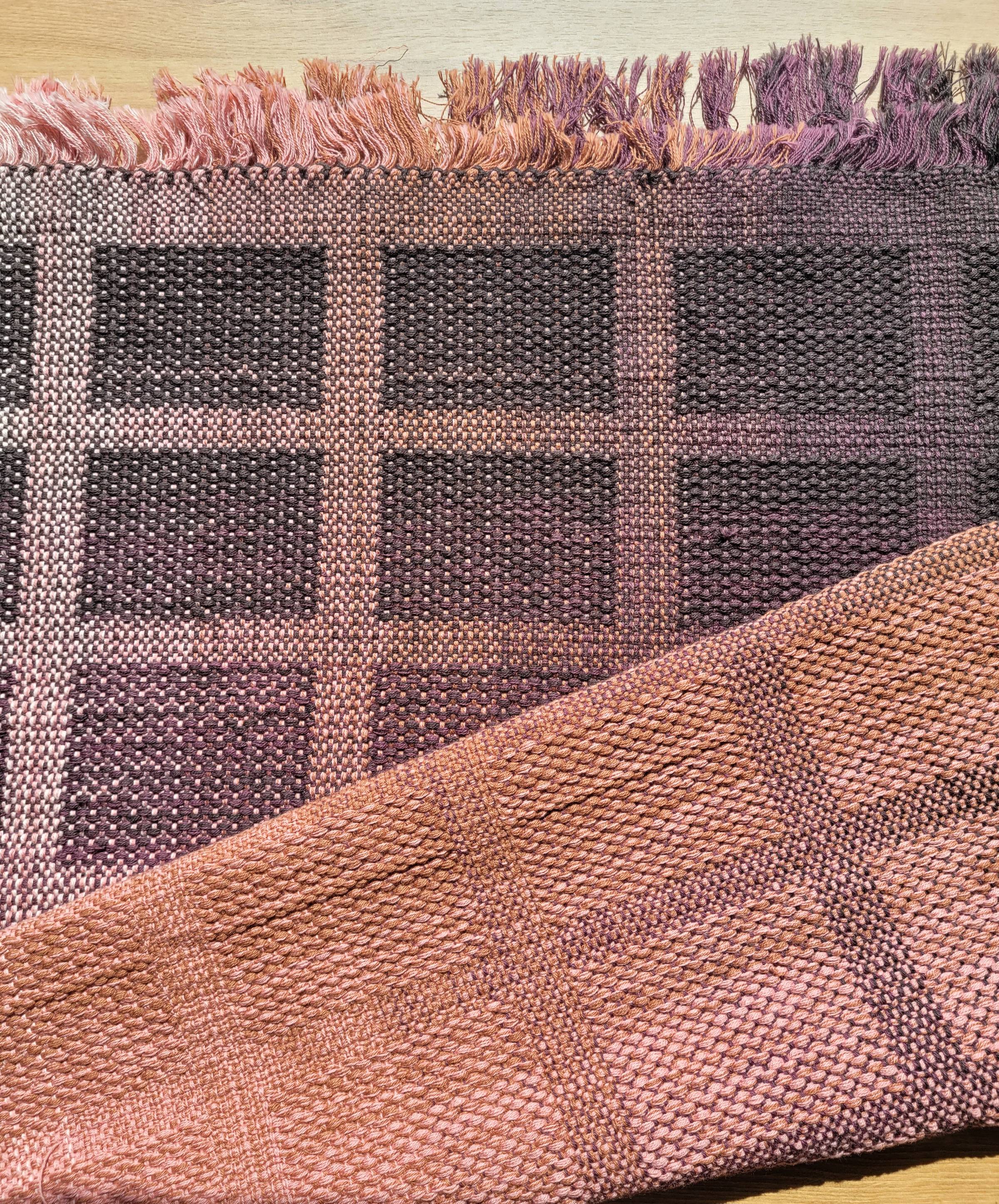 Handwoven fabric in a brick-style summer-and-winter block pattern. Both warp and weft are a gradient from light pink to dark brown, and the brick squares contrast against the surrounding weaving.