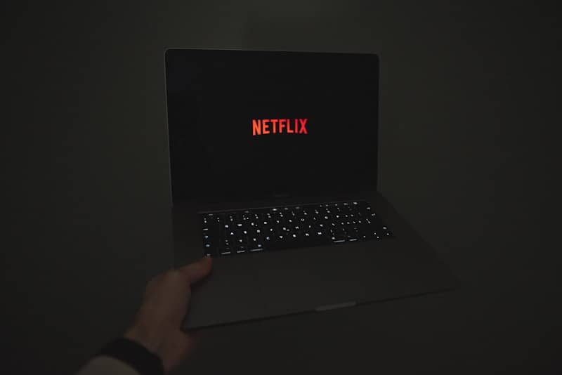 a person holding a laptop with the word netflix on the screen