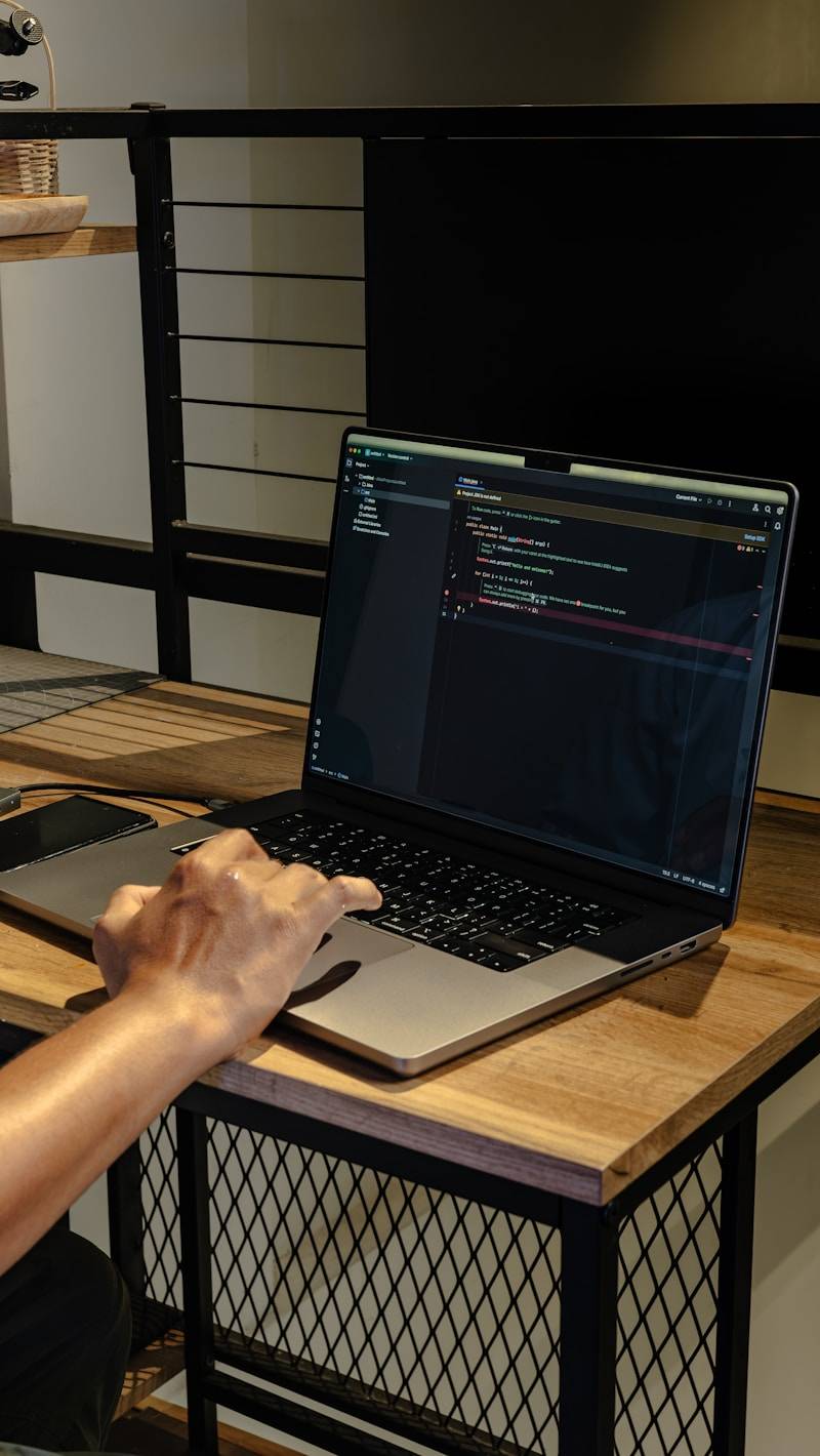 A person typing on a laptop with code on screen.