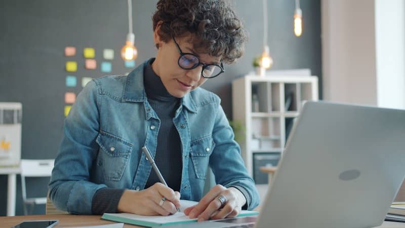 Woman with glasses writing in notebook at desk