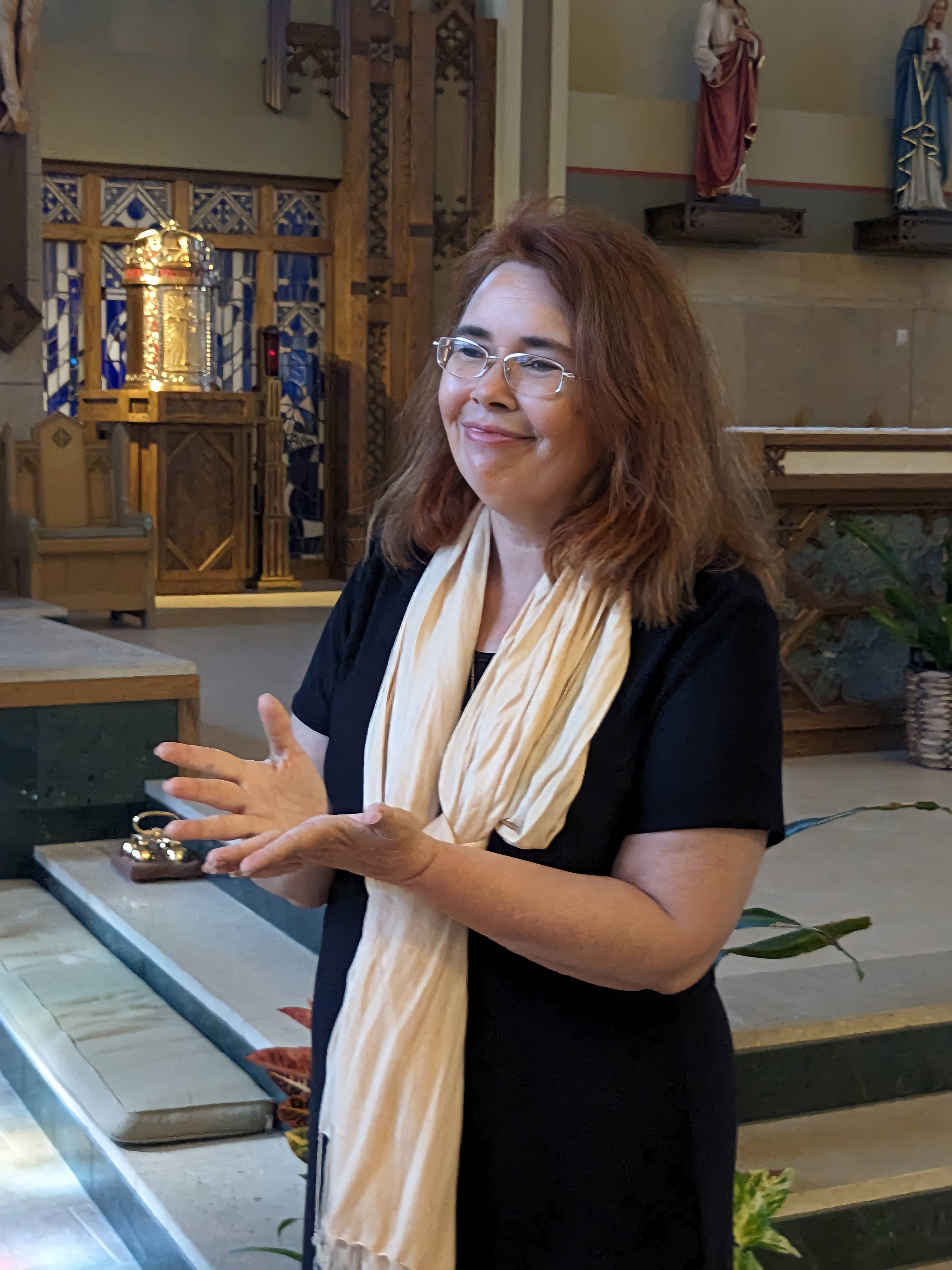 A brown-haired woman with glasses smiles near a Catholic tabernacle
