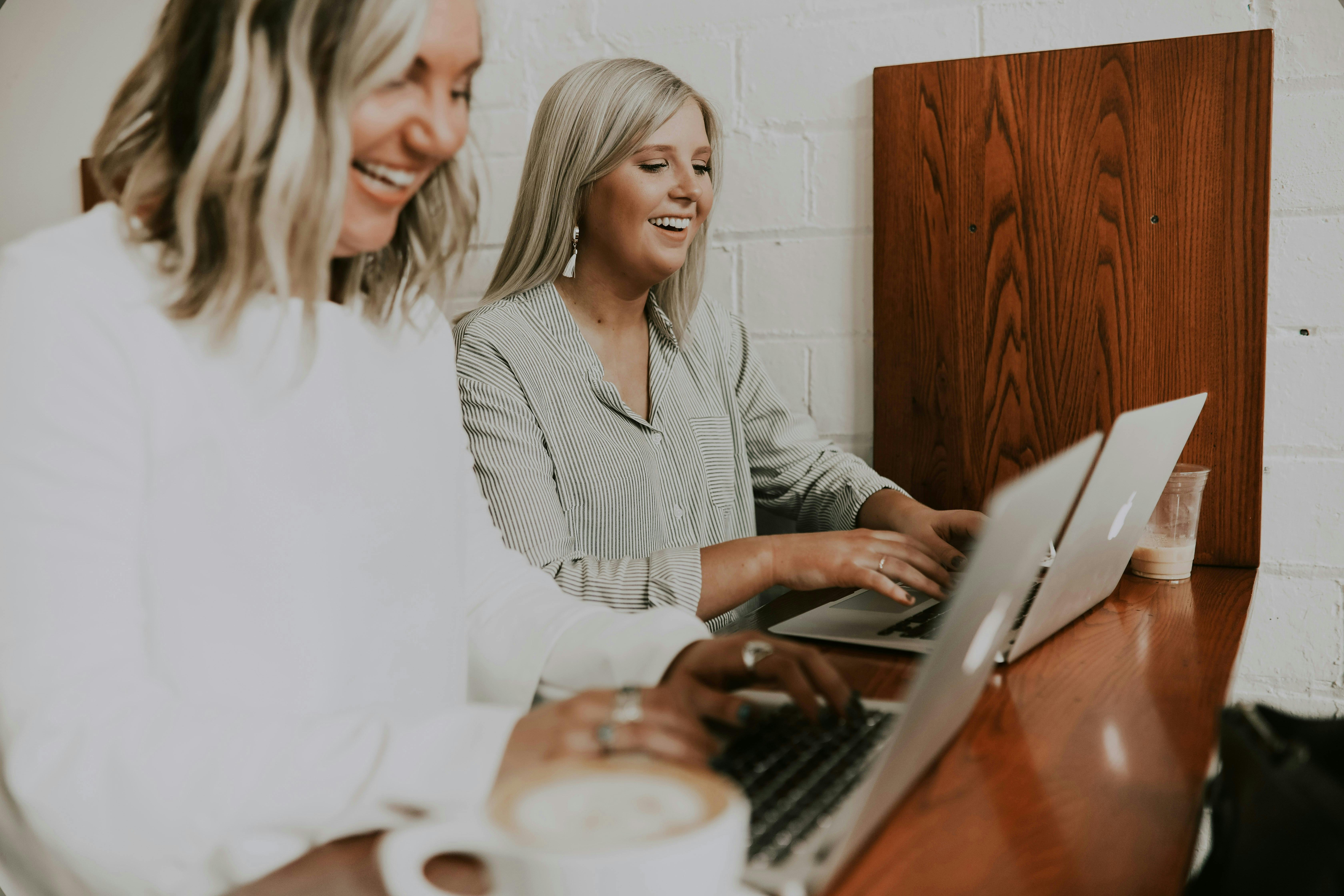 Two women working on laptops, smiling