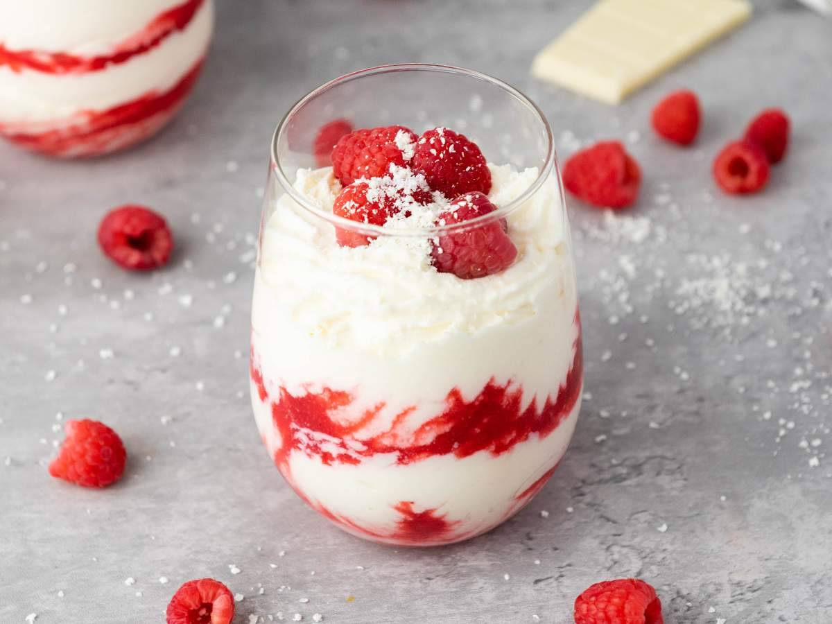 A glass of white chocolate mousse on a grey surface.