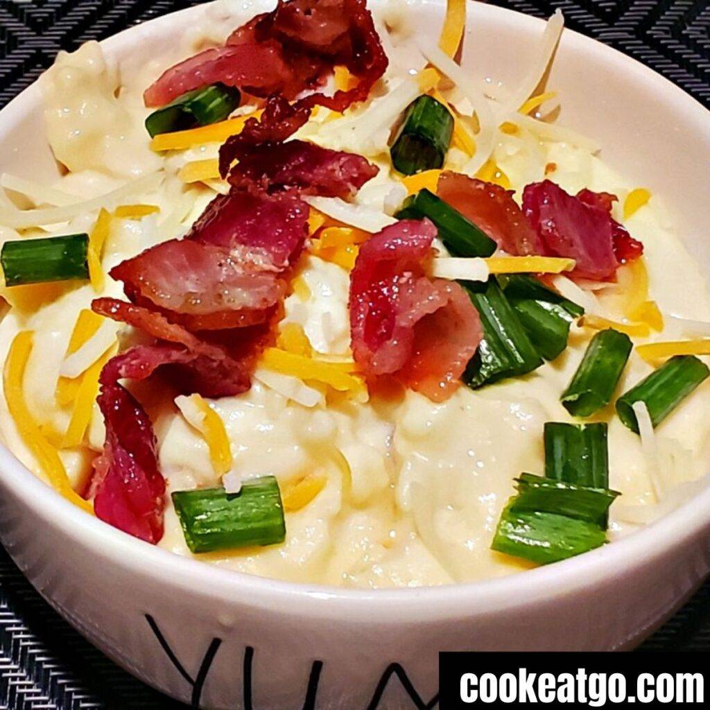 A bowl of mashed potatoes with small bacon bits.
