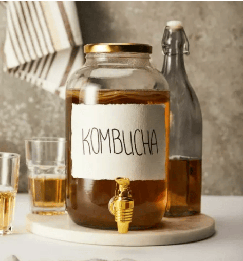 A clear glass jar labeled “KOMBUCHA” filled with a brown liquid, placed on a wooden tray