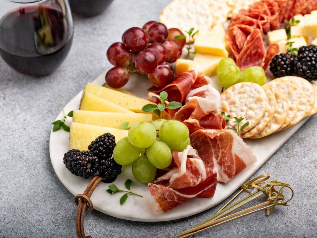 A charcuterie board with two glasses of red wine in the background.