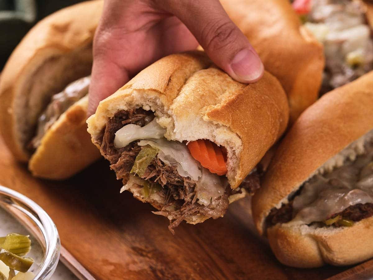 Italian beef sandwich being held over a wooden board.