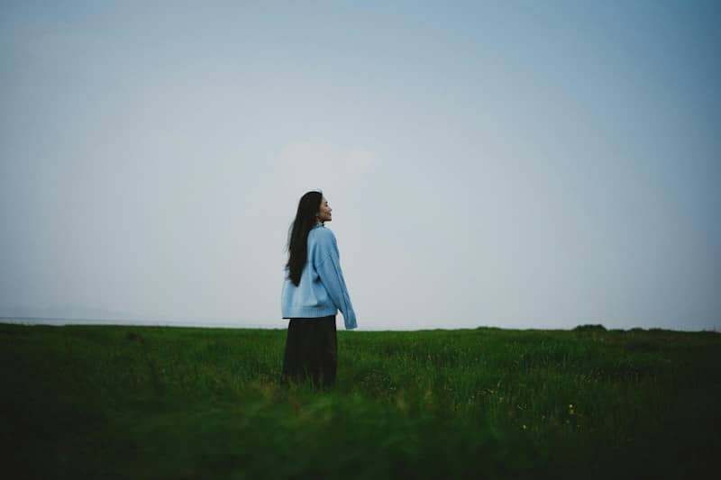 A woman stands in a grassy field looking up