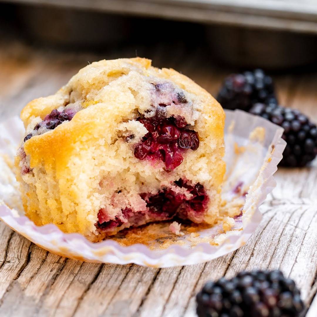 Bitten blackberry muffin in a paper liner. Gray wooden surface. 