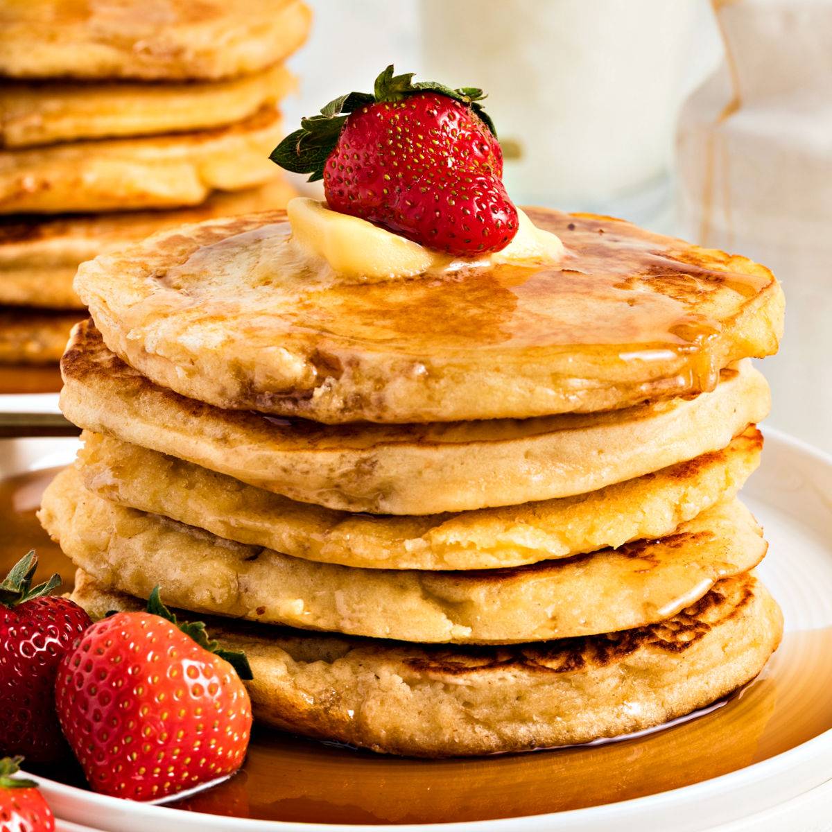 Stack fo pancakes with syrup and strawberries. 