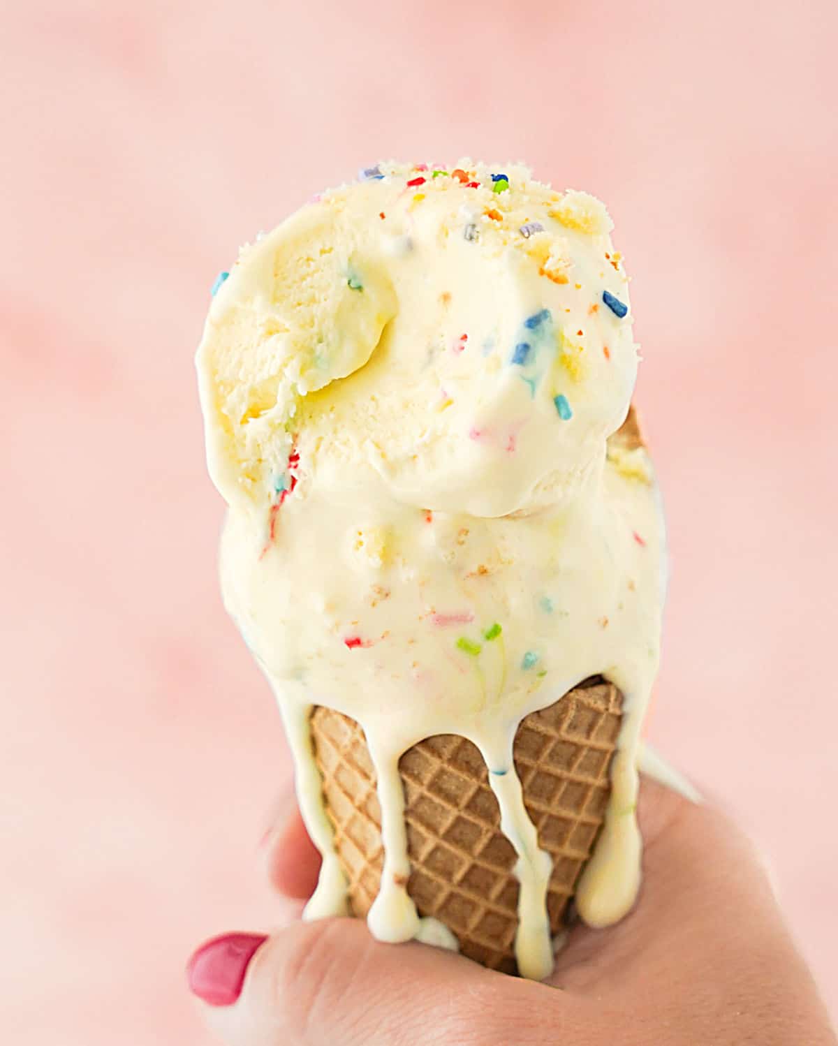 Waffle cone with dripping funfetti icre cream. Pink background. 