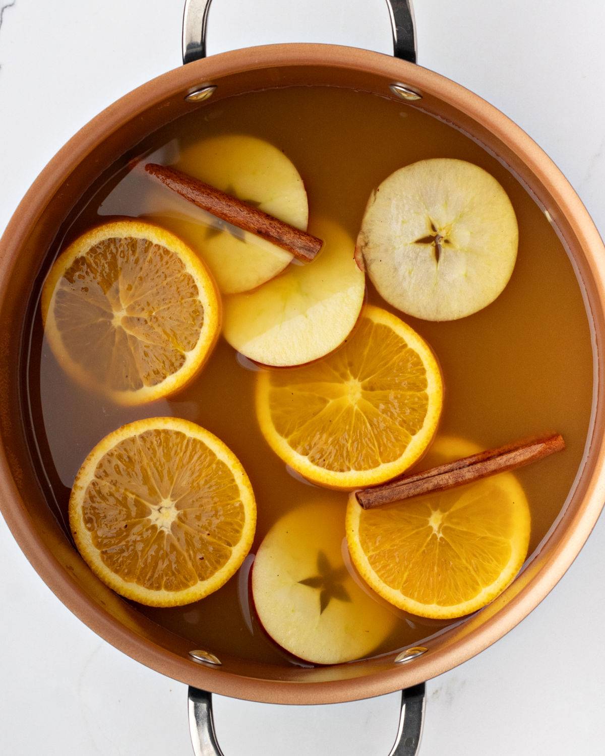 Copper pot with apple cider and sliced fruit. 