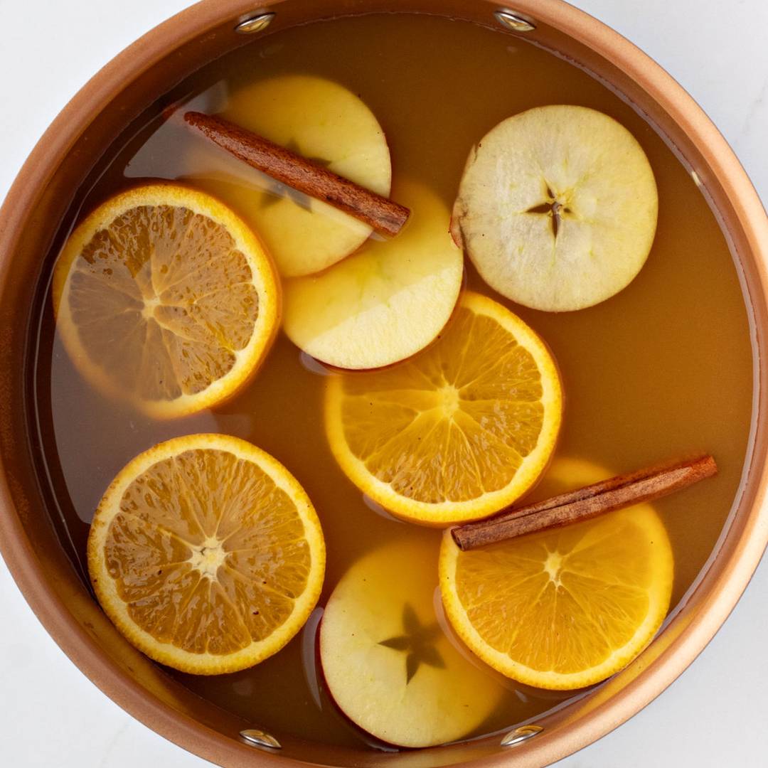 Copper pot of apple cider with sliced fruit and cinnamon.