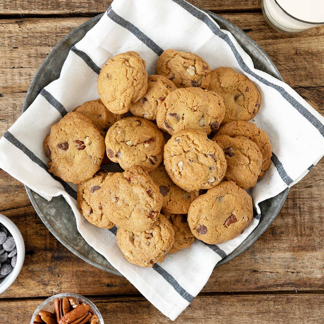 Pile of pecan chip cookies on a gray striped towel.