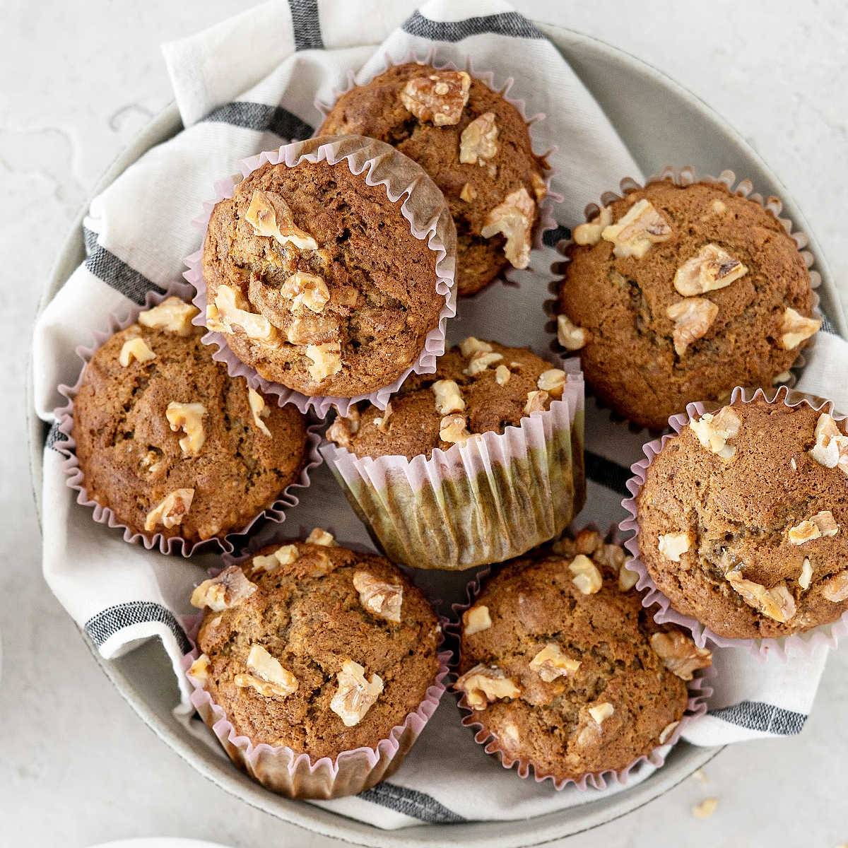 Pile of banana nut muffins on a striped white and gray towel.