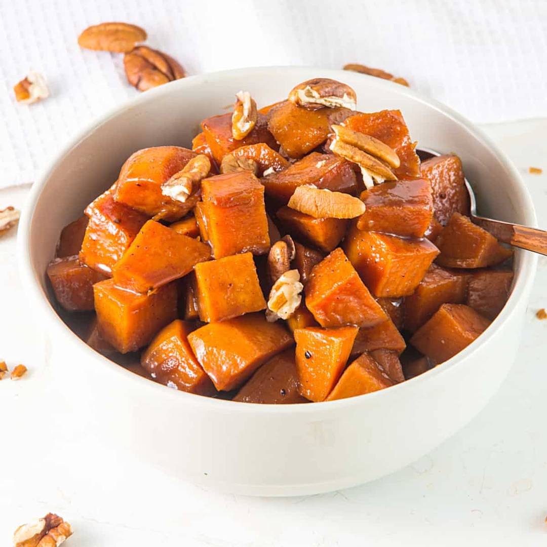 White bowl of candied sweet potatoes with pecans.