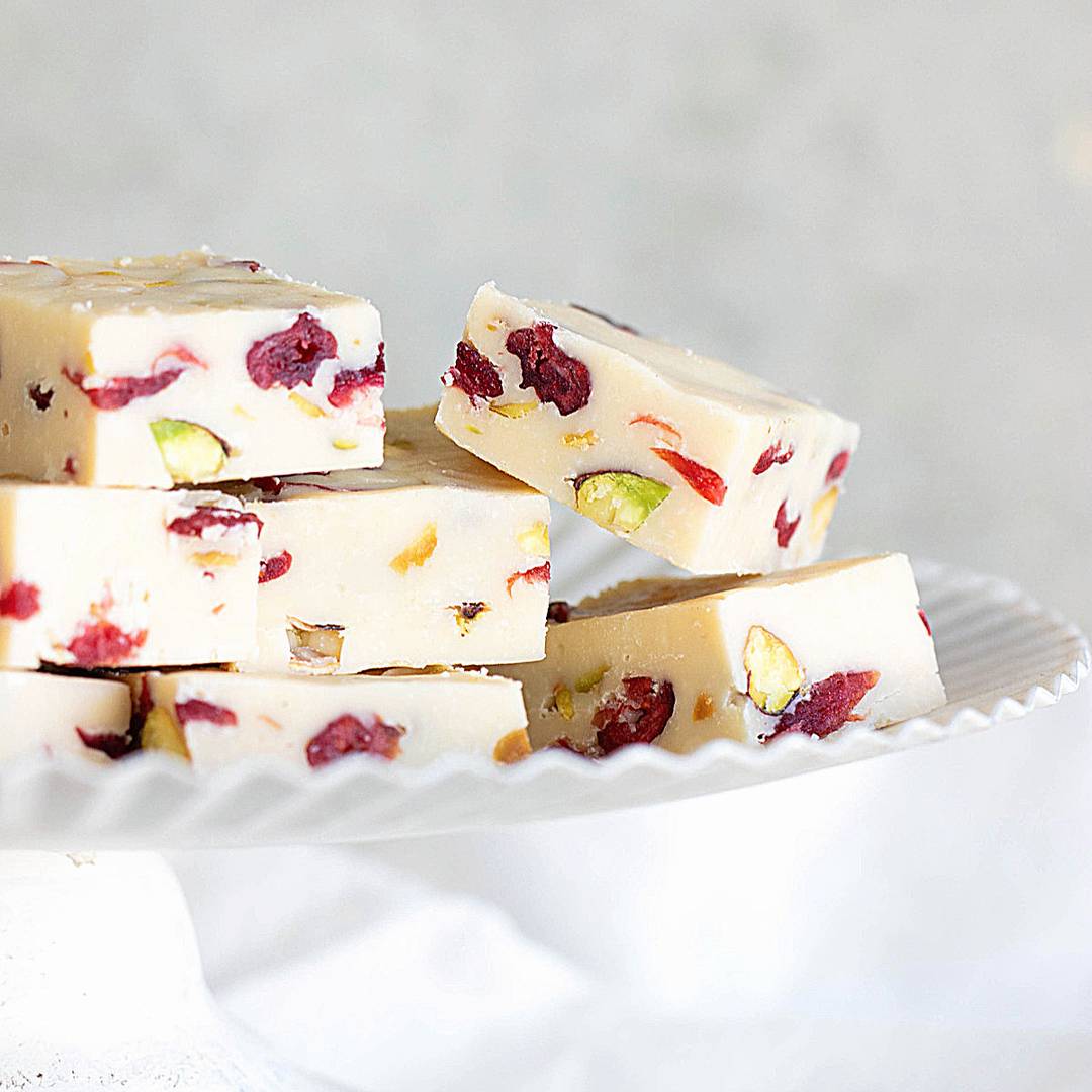 Pieces of white pistachio cranberry fudge on a white cake stand.