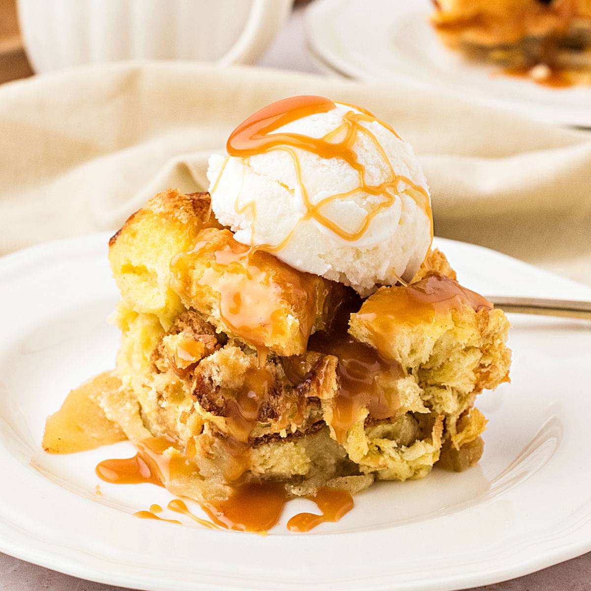 Serving of bread pudding with ice cream and caramel on a white plate. 
