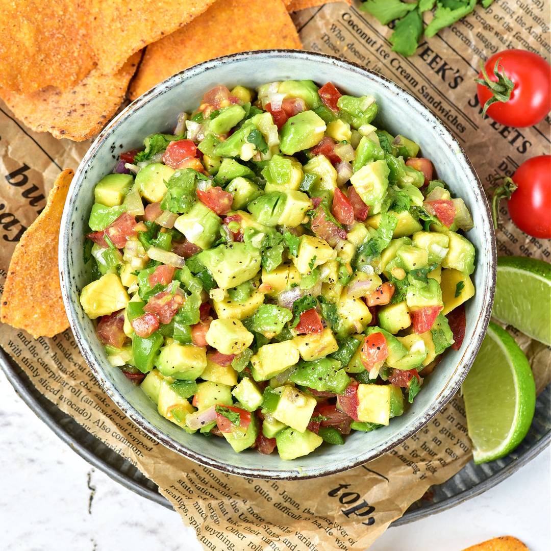 Gray bowl with avocado salsa. Chips and lime wedges.
