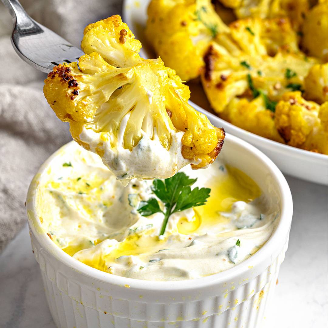 Spicy cauliflower bites with dip in white bowl.
