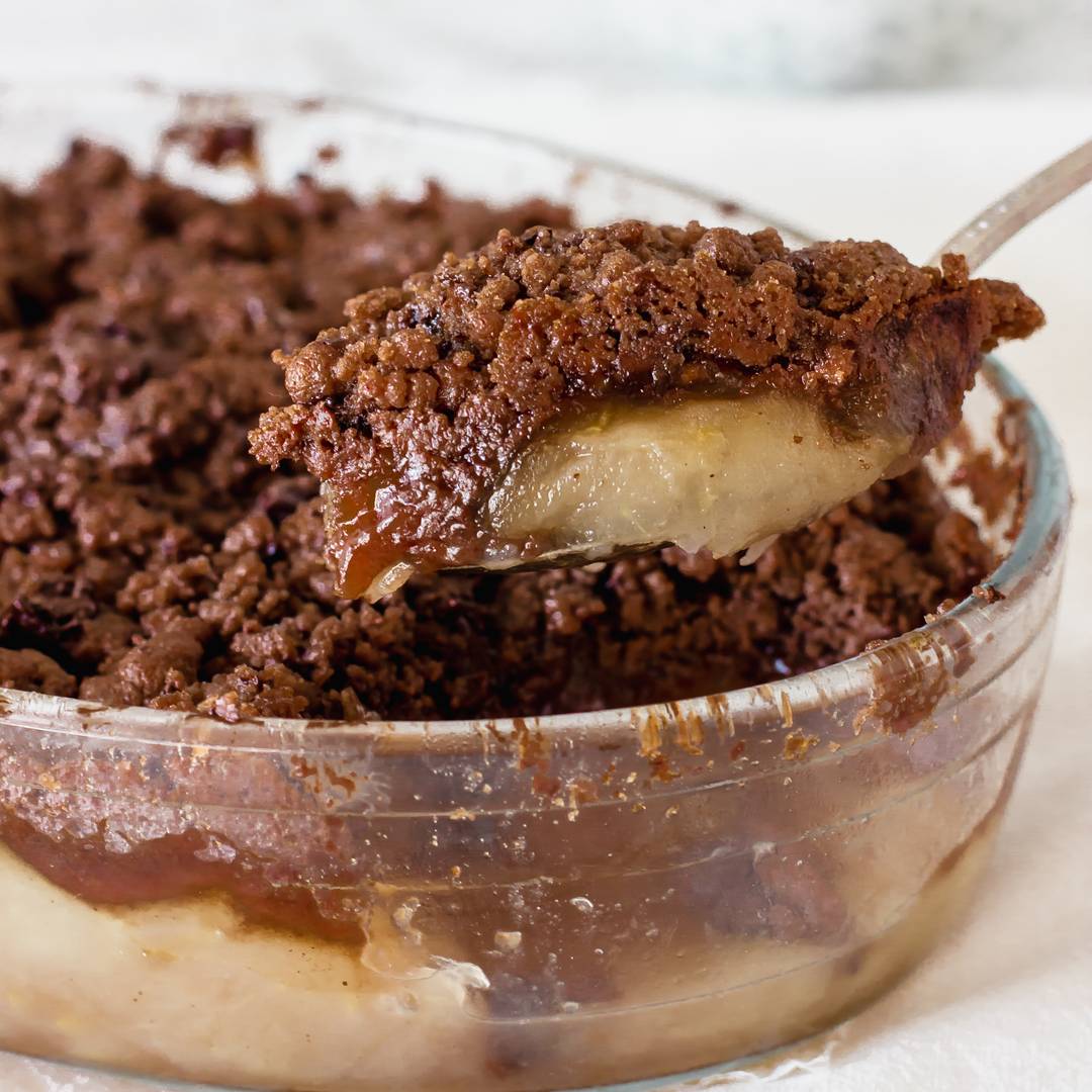 Glass dish with apple chocolate crisp lifted with a spoon.