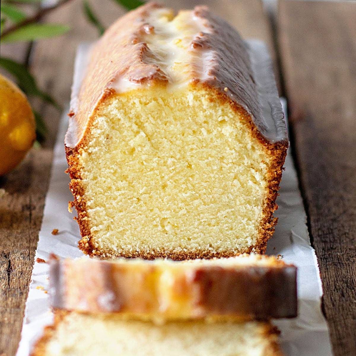 Glazed lemon pound cake on a white paper and wood suface. Some cut slices.