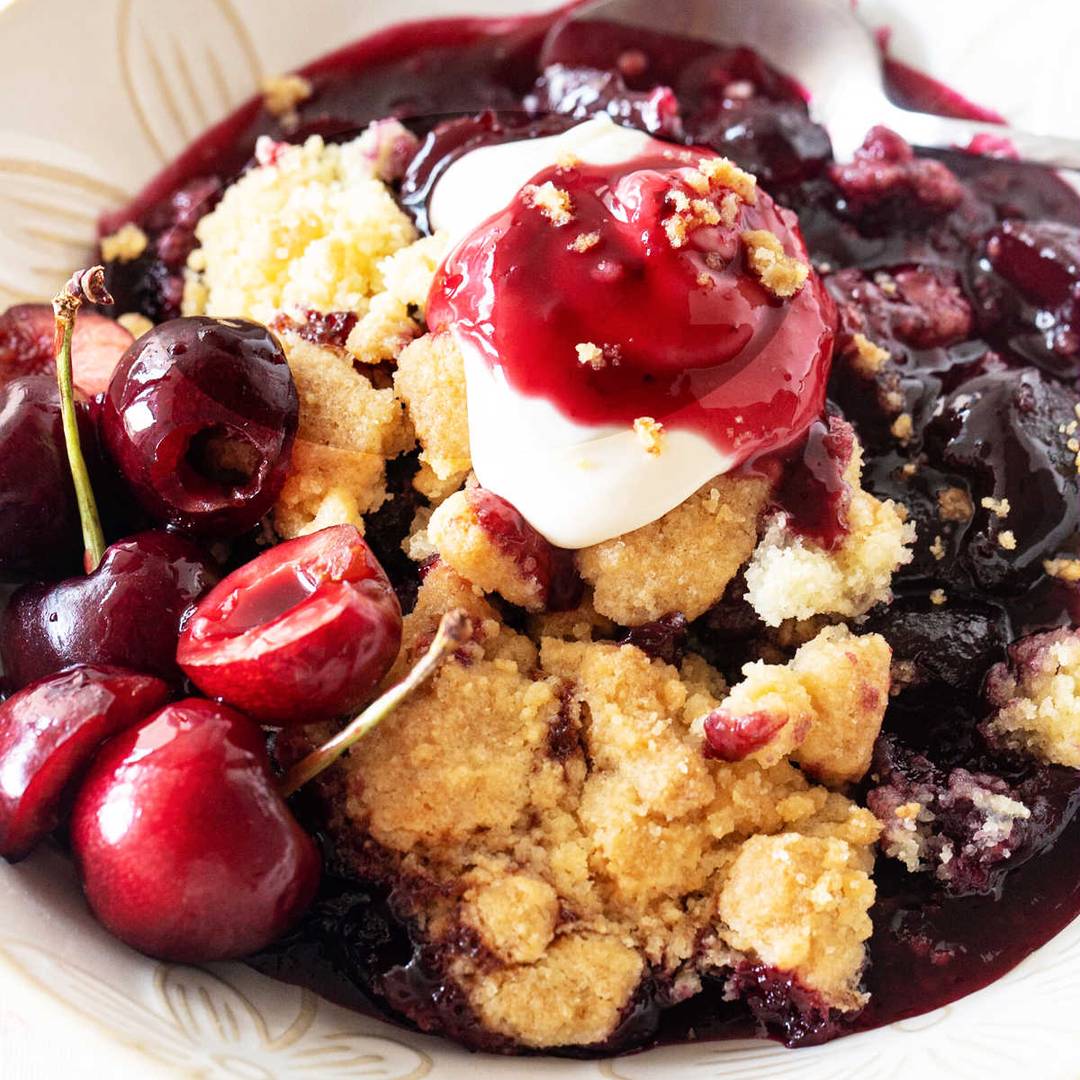 Bowl of cherry dump cake with cream.