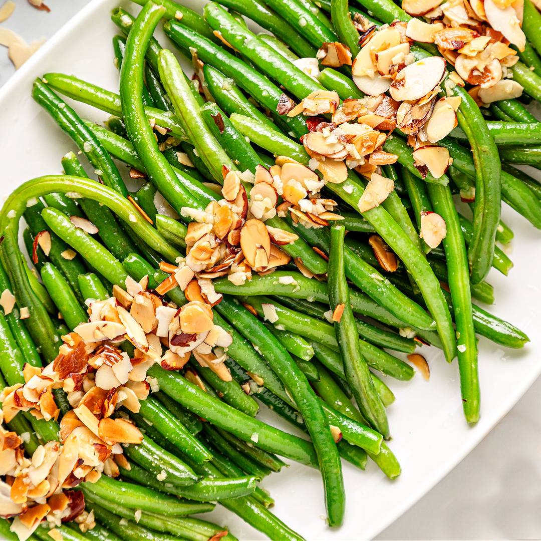 Green beans with almond topping on a white plate.