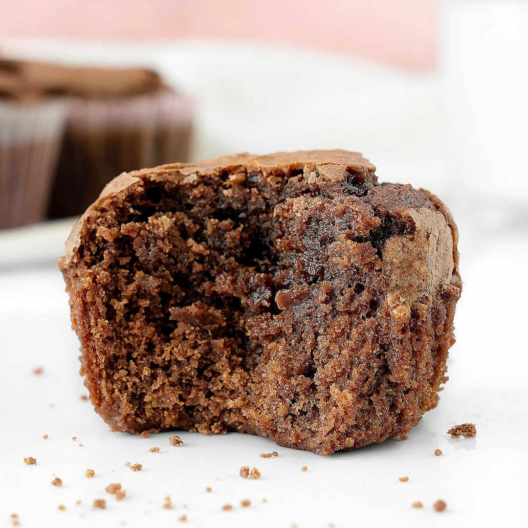 Bitten brownie muffin on a white surface.