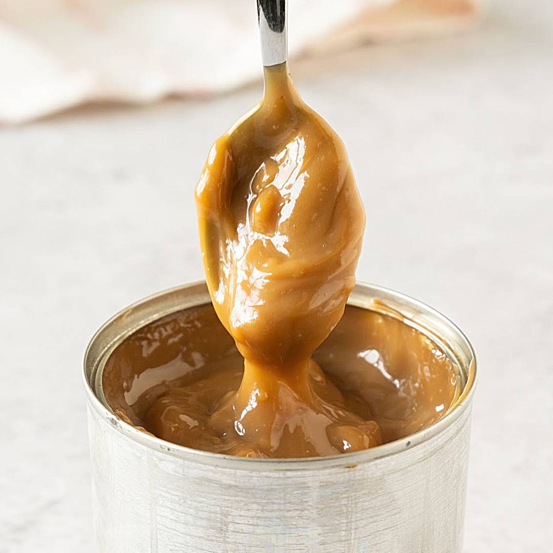 Spoon lifted from can with dulce de leche. 