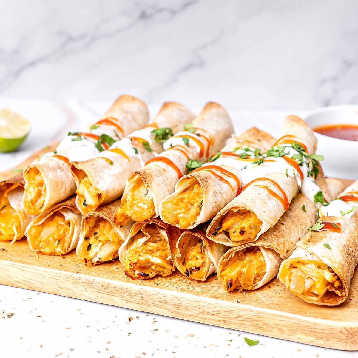 Rows of stacked chicken taquitos on a wooden board. 