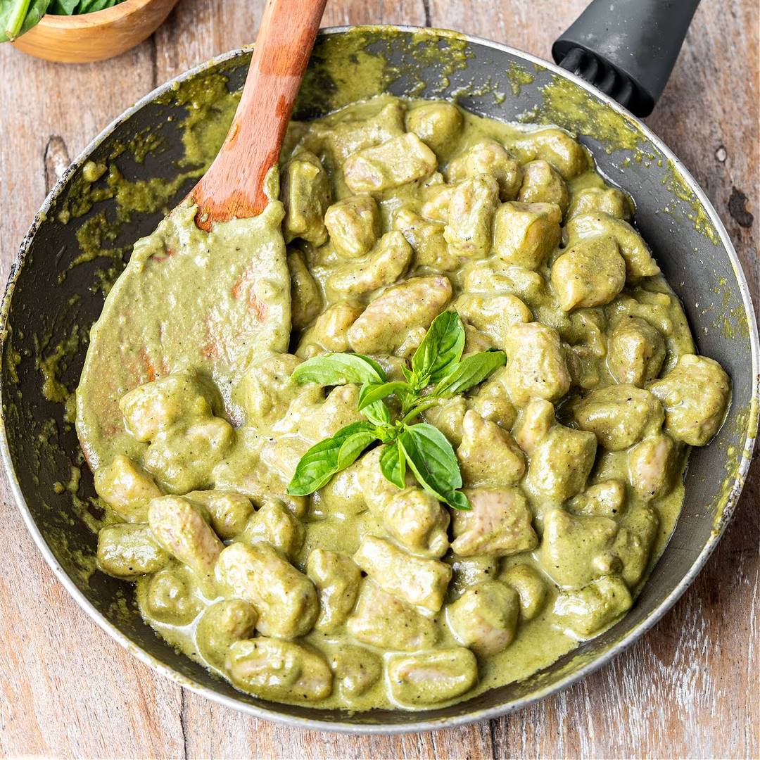 Skillet with pesto gnocchi. Wooden spoon. Basil leaves.