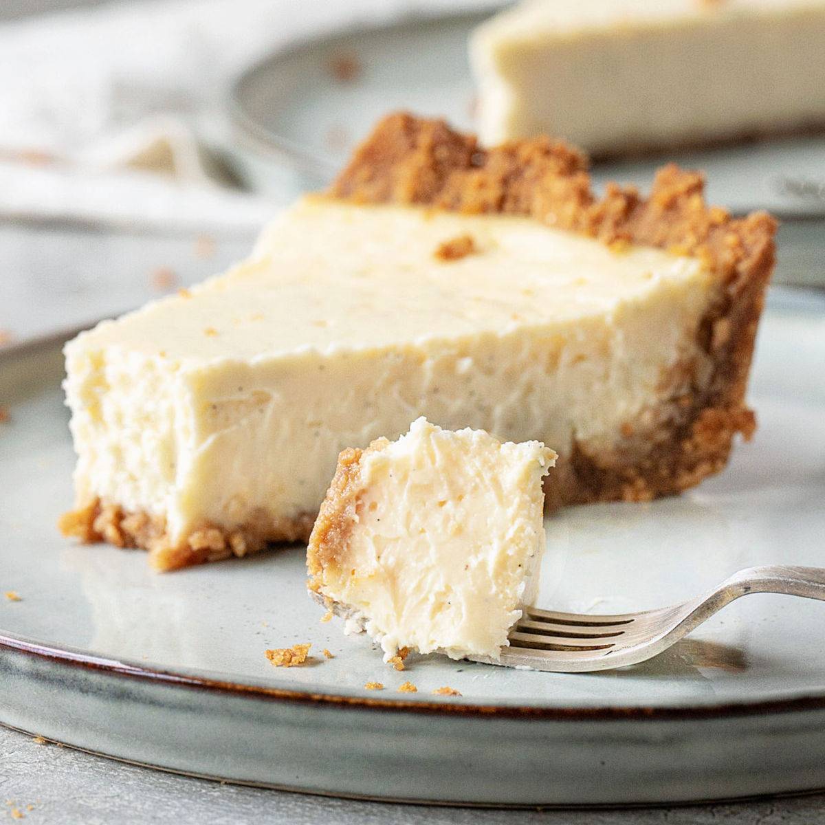 Slice of cheesecake pie on a light gray plate. Fork with a bite.