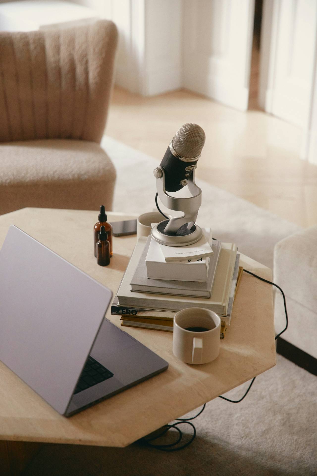 A picture of a laptop and a pile of books with a podcasting mic on top