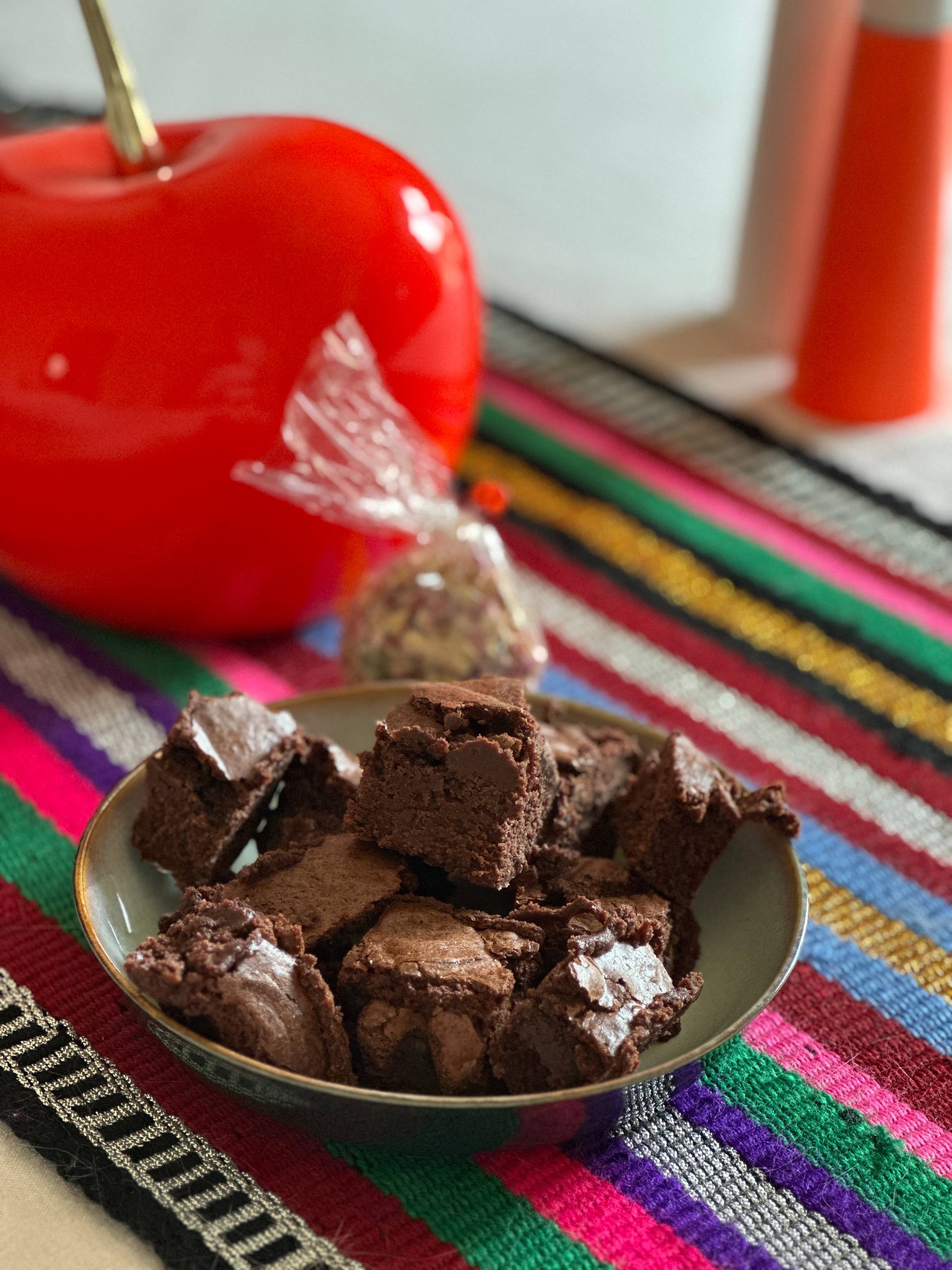 A plate of brownies and rose petals in a small plastic bag, on top of a bright striped table runner