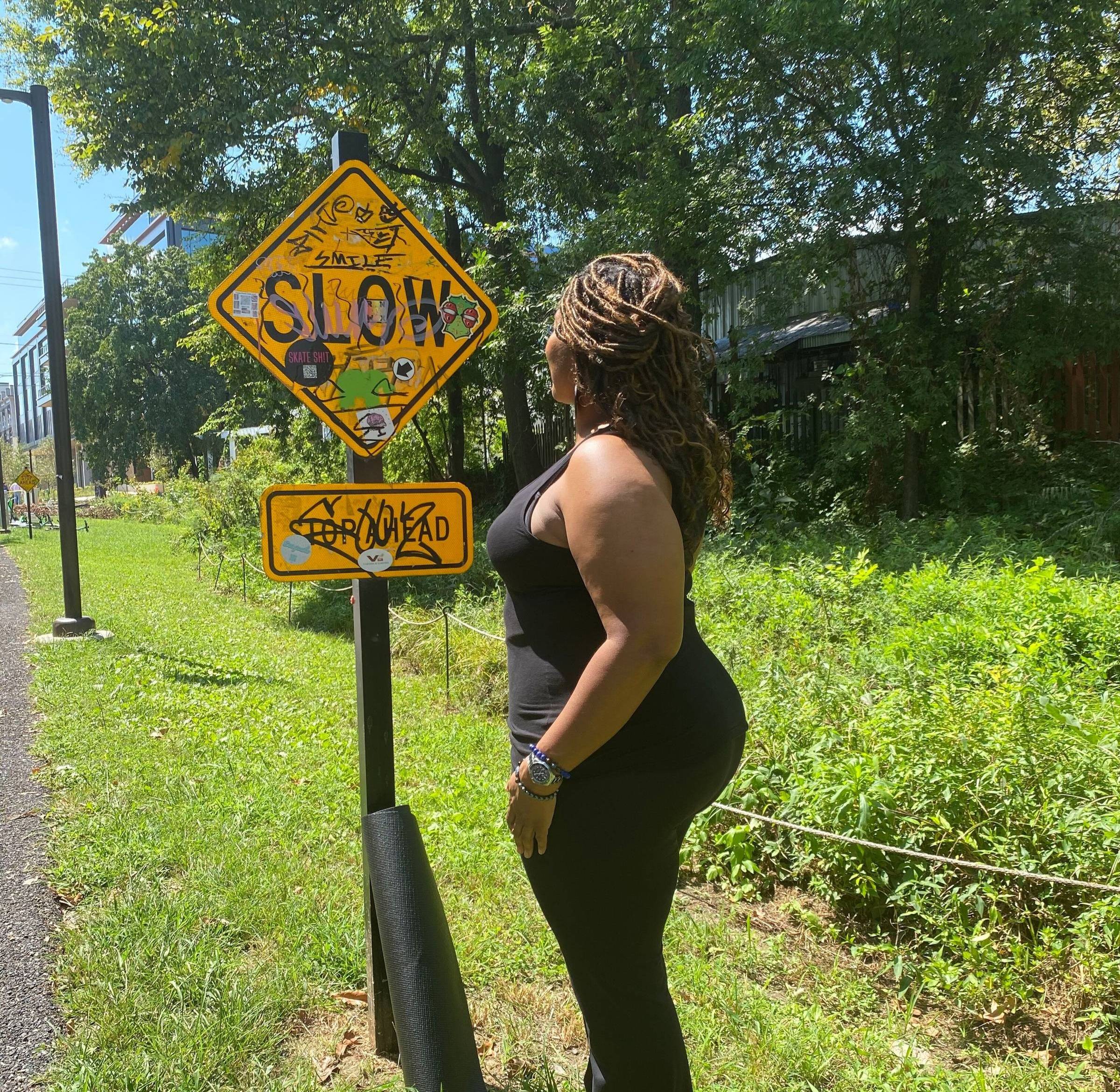 Anika Apple looking at a yellow street sign that reads 'slow.'