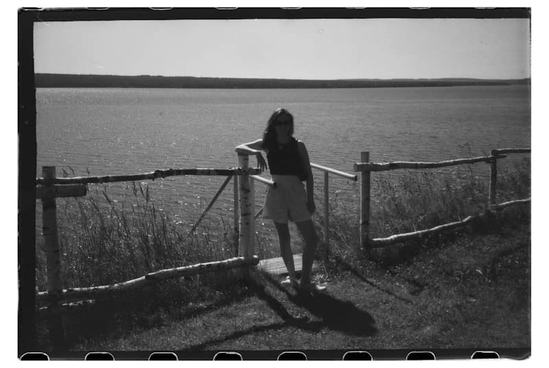 A woman leaning on a rustic wooden fence overlooking a large lake