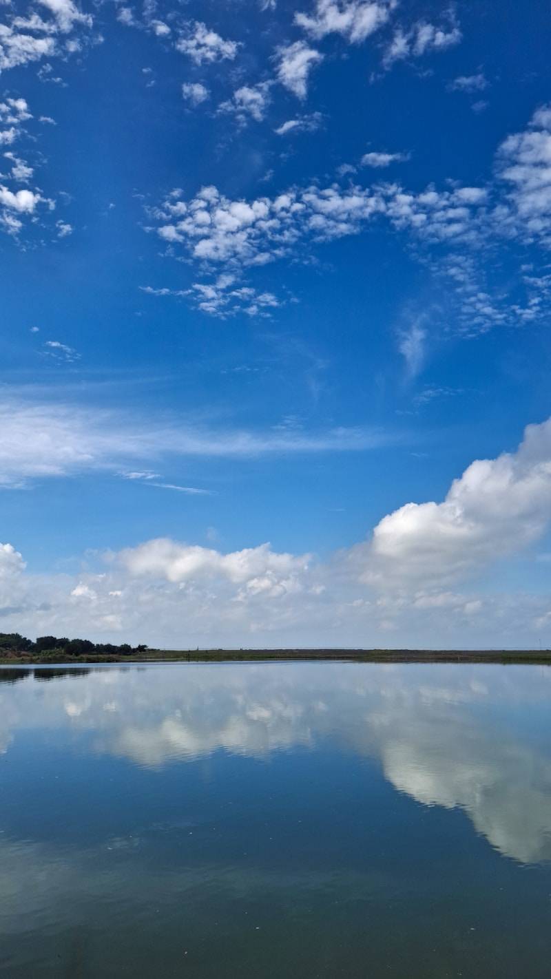 Calm water reflects a bright blue sky with scattered clouds.