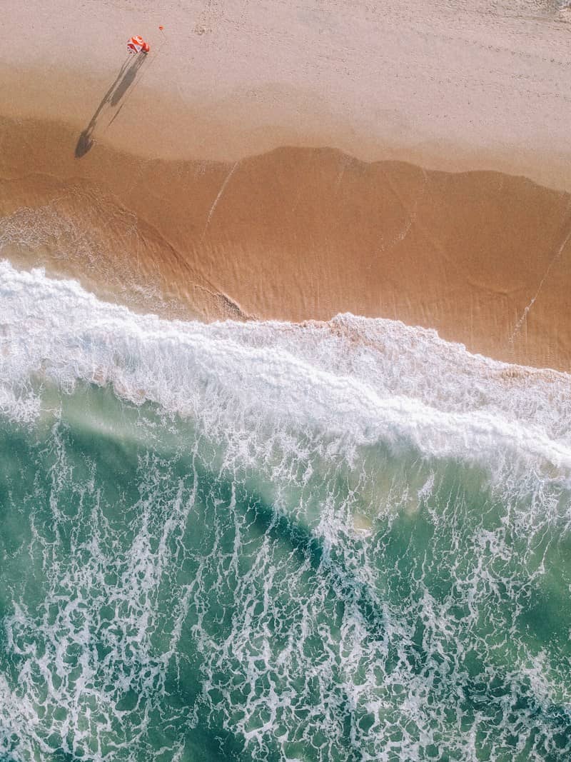 Person walking on a sandy beach with crashing ocean waves.