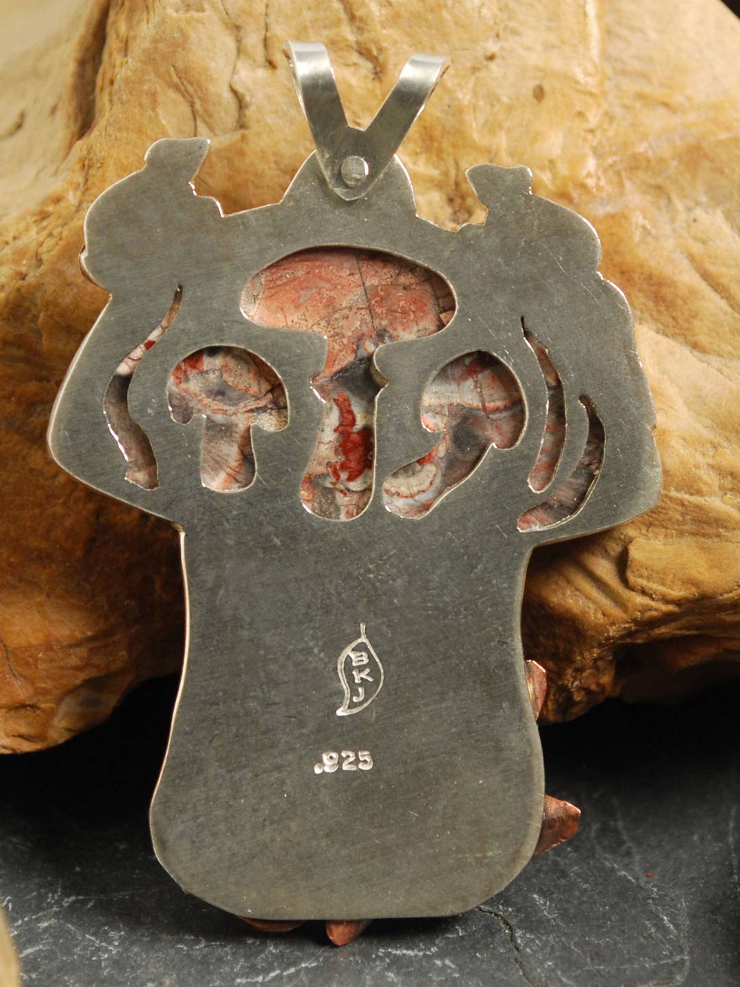 Back of mushroom pendant with cut out mushrooms behind stone