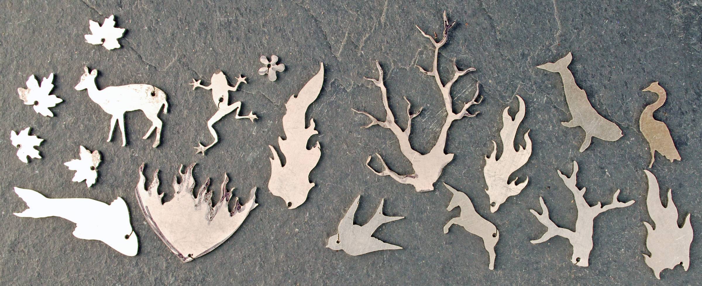 A group of silver shapes that were cut out from backs of pendants including animals, fish, trees, flames