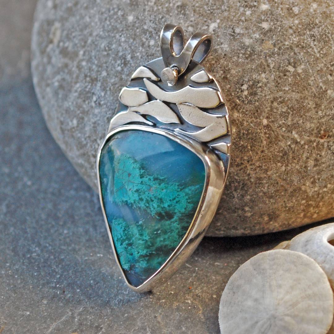 Silver pendant with chrysocolla and silver decoration above the stone that looks like water ripples