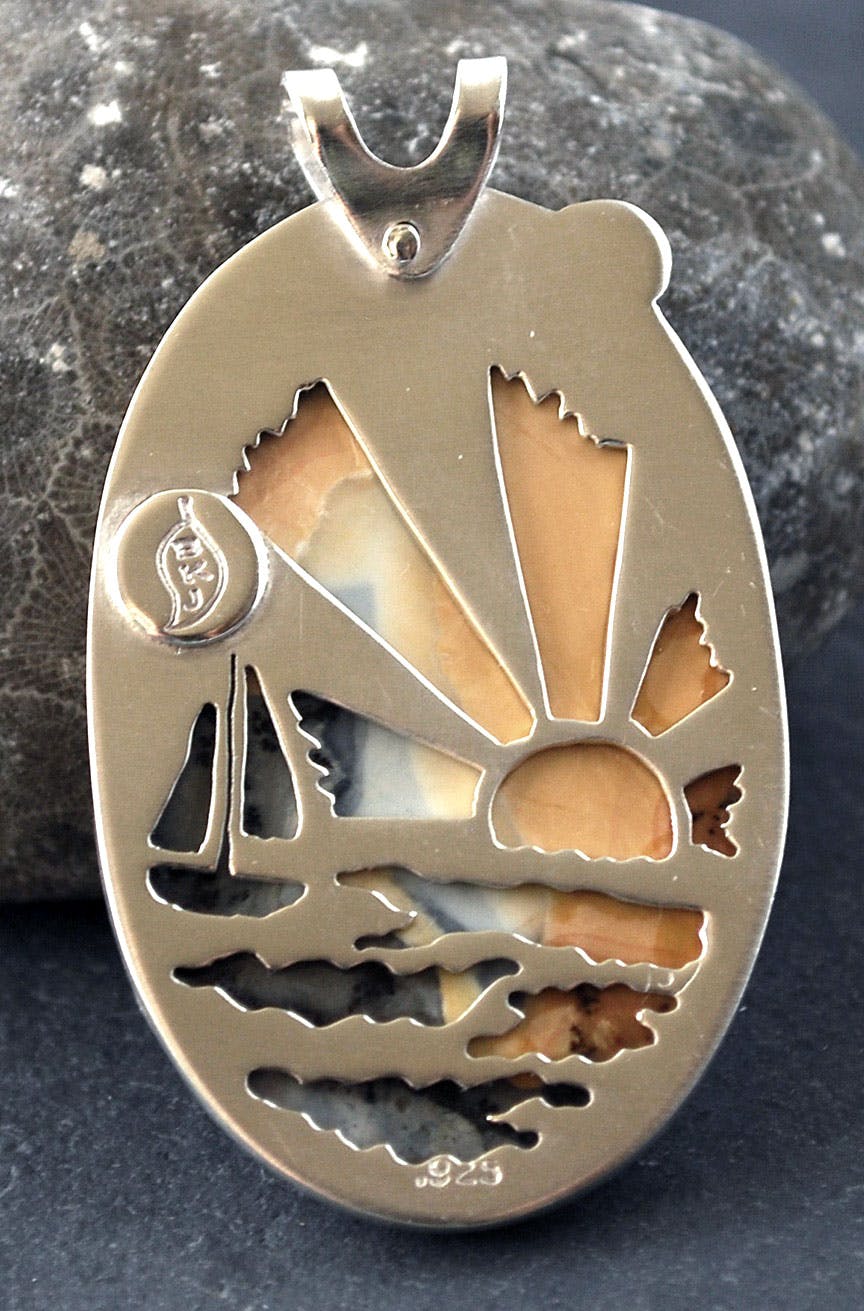 Back of pendant cut out of sailboat on water with setting sun