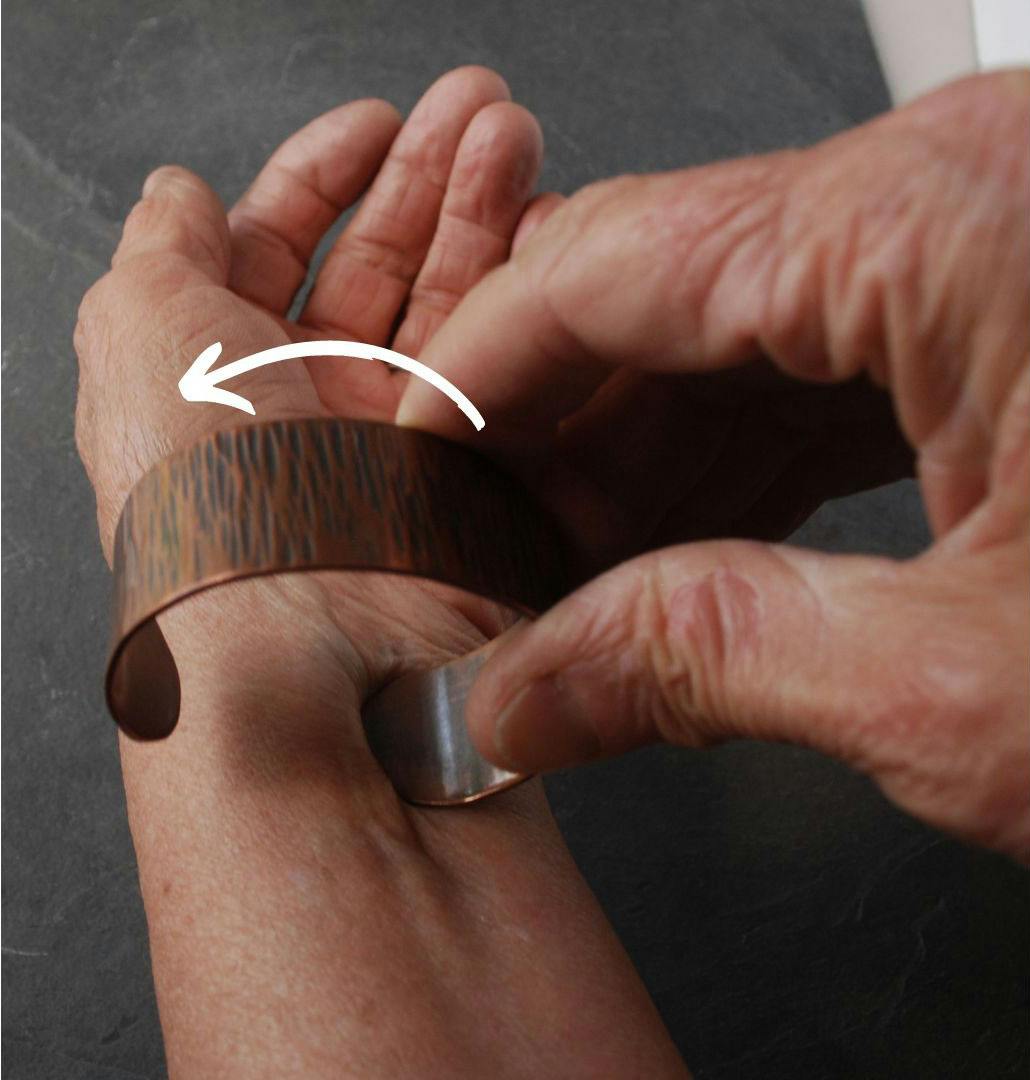 pressing the end of a cuff into the inner wrist with arrow showing direction to turn cuff around arm