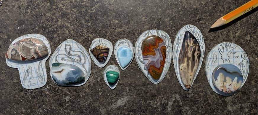 A series of stones sitting on roughly sketched pendant designs