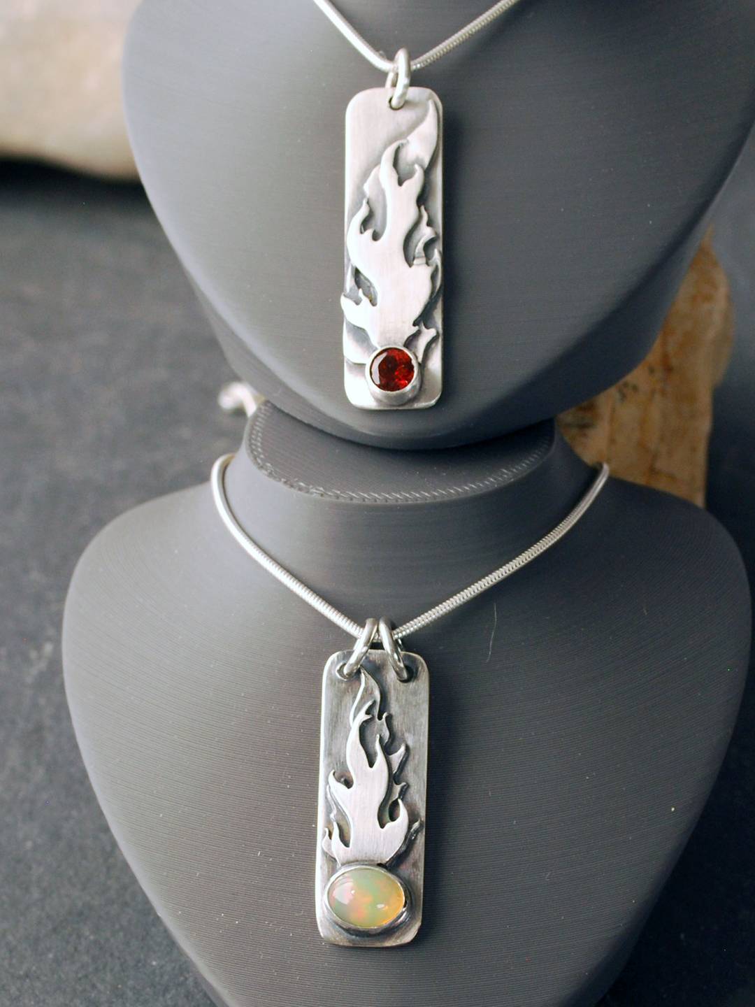 Two vertical bar pendants with flames, top one with garnet, bottom one with opal