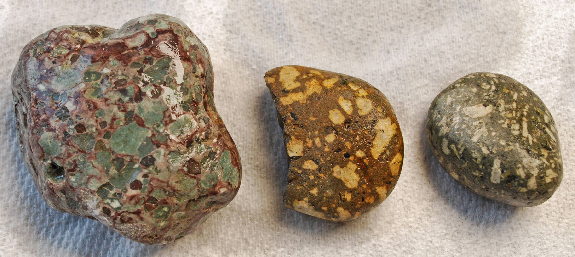 Three rough brecciated rocks; one has green clasts and brown matrix,  one is brown and beige, the other is gray and white