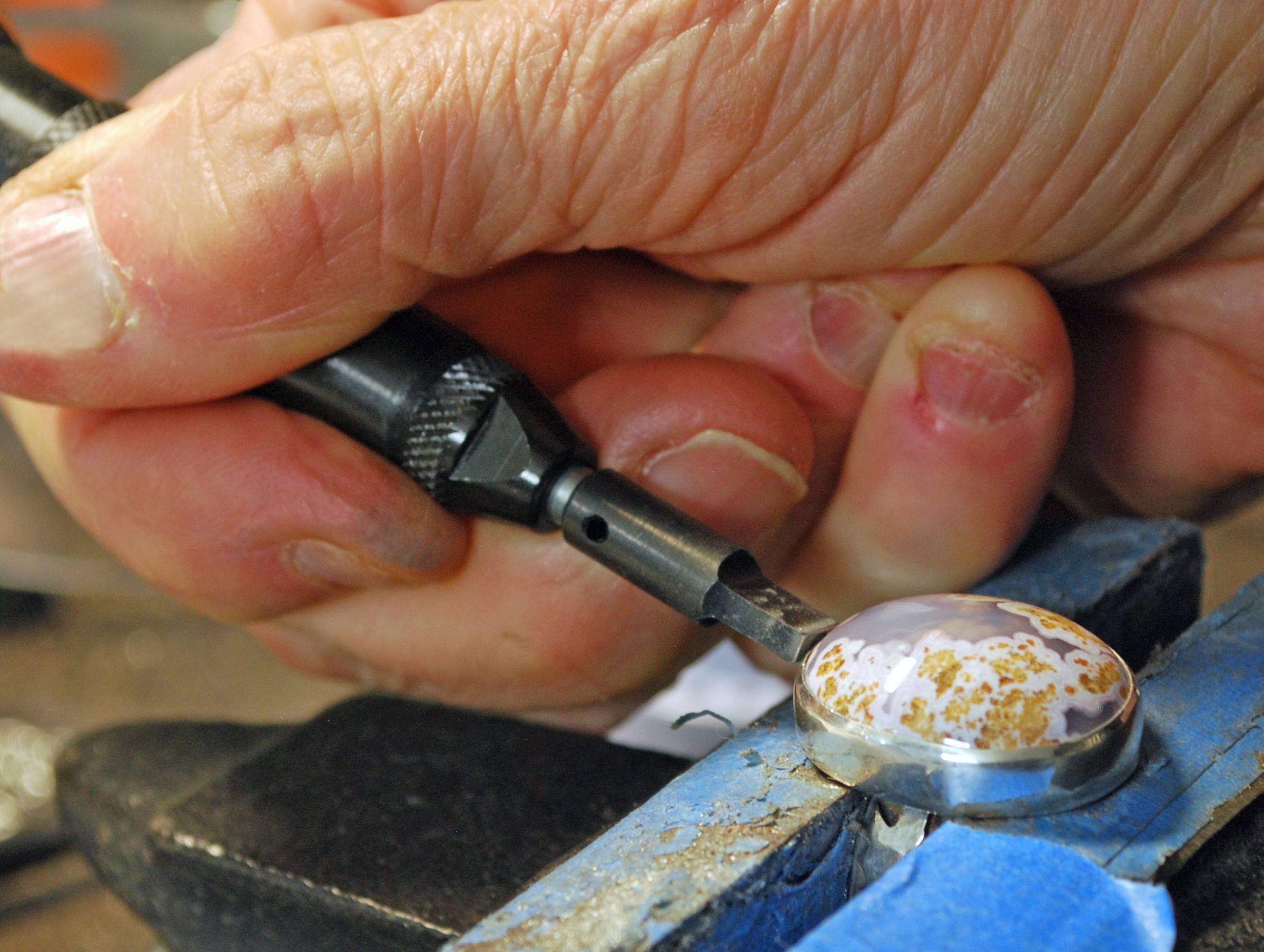 Hand holding hammer handpiece tip against a stone and bezel