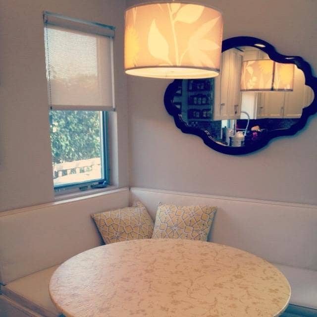 A cozy window seat with soft pillows, a blue scalloped mirror and warm lamplight